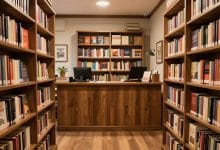 Interior aconchegante de uma livraria virtual em um jogo de simulação, com estantes repletas de livros, balcão de atendimento e decoração acolhedora